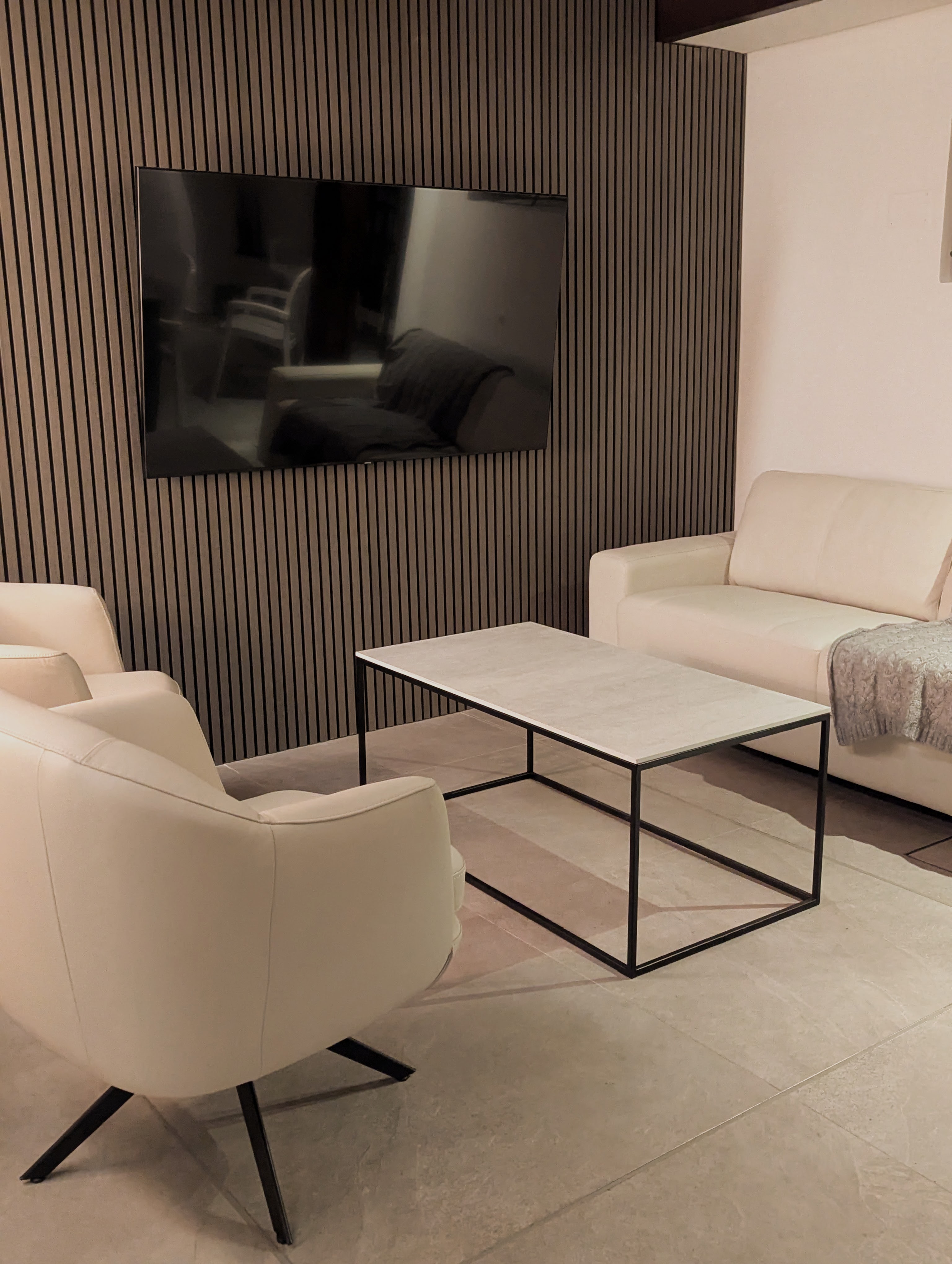 Fotografía del estar con panel ranurado, sillones y mesa de centro
